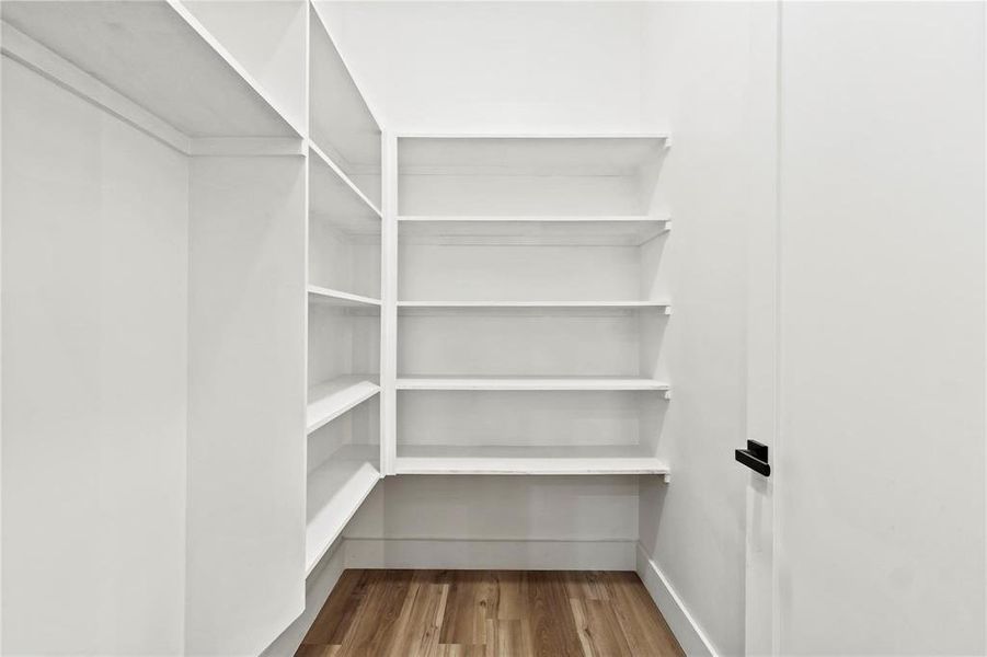 Walk-in pantry with extensive built-in shelving, white finishes, and wood-finish flooring