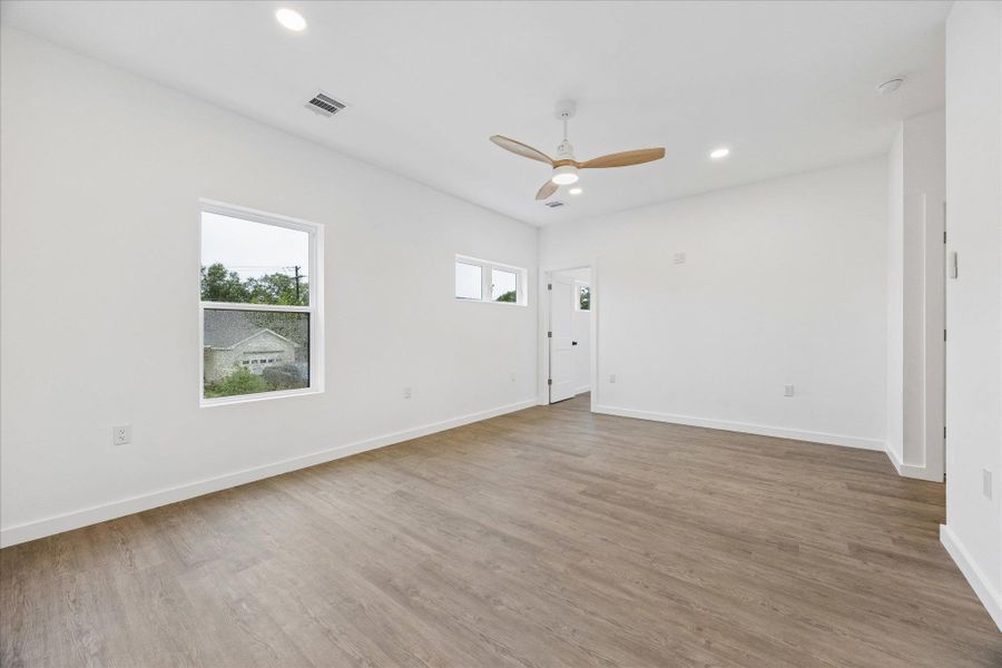 Wood-look flooring and ample windows create an inviting, open atmosphere in this naturally illuminated bedroom.