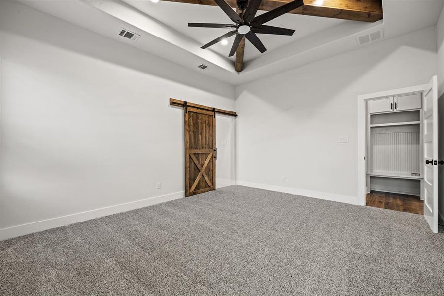 Unfurnished bedroom with dark colored carpet, visible vents, baseboards, and a barn door