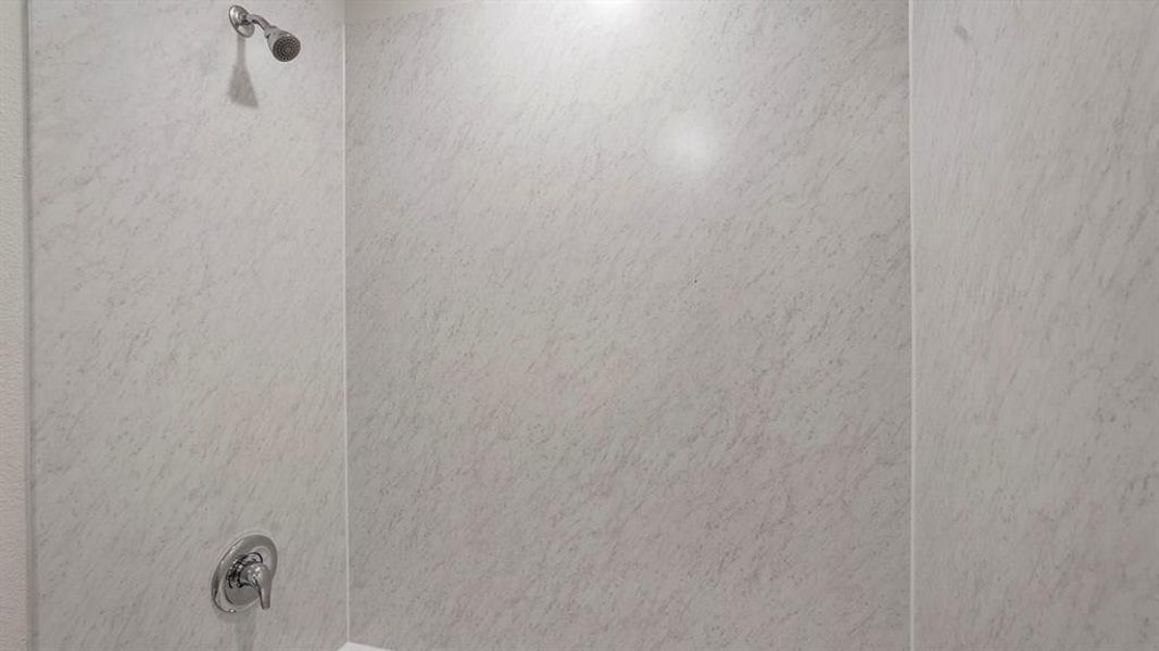 Shower stall featuring light-toned, textured wall panels and chrome fixtures