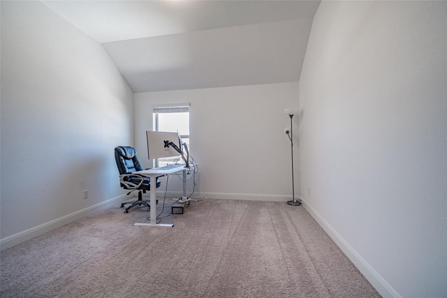 An airy office space offers vaulted ceilings, soft carpeting, and a sun-filled window, perfect for productivity.