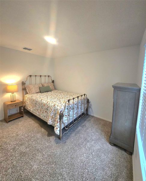 Carpeted room with white walls, featuring a ceiling light fixture and a wall vent