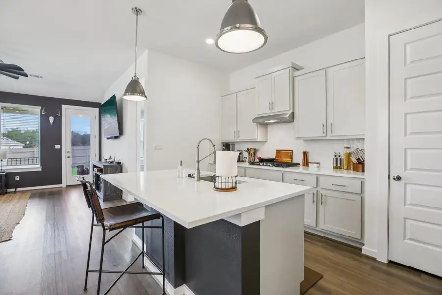 Kitchen featuring dark wood-style floors, backsplash, decorative light fixtures, a kitchen island with sink, and a breakfast bar Kitchen featuring dark wood-style floors, backsplash, decorative light fixtures, a kitchen island with sink, and a breakfast bar