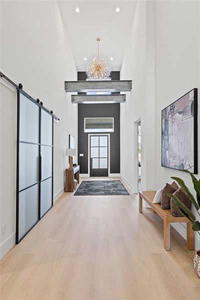 Entryway featuring a barn door, a high ceiling, recessed lighting, light wood-style flooring, and a chandelier