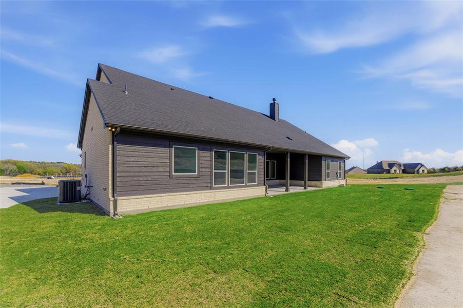 Back of property with a patio area, a yard, brick siding, a chimney, and a shingled roof