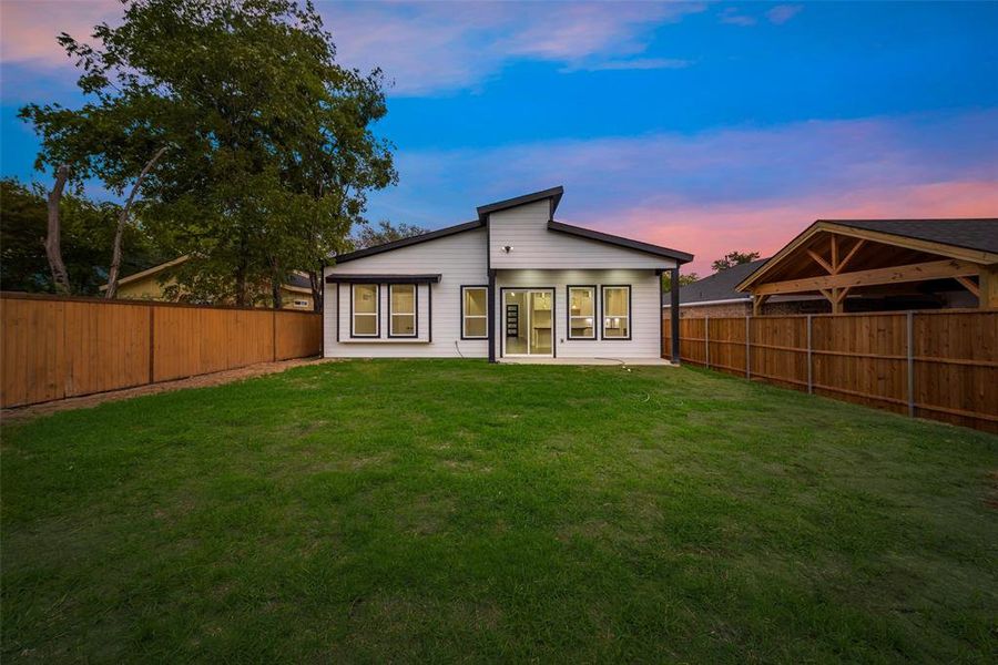 Back house at dusk featuring a lawn