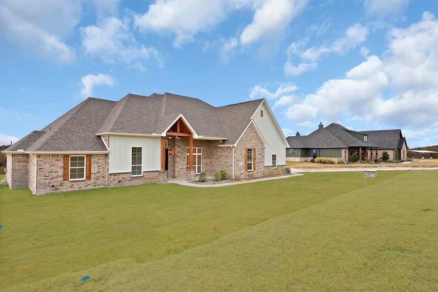 View of front of property with a front yard, a shingled roof, board and batten siding, and brick siding View of front of property with a front yard, a shingled roof, board and batten siding, and brick siding