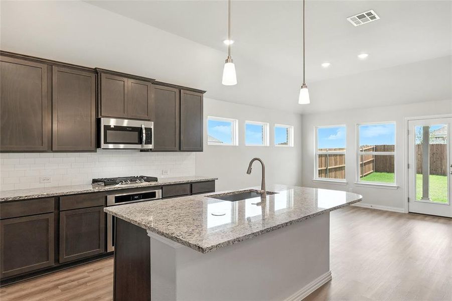 Kitchen featuring light wood-type flooring, dark brown cabinets, stainless steel appliances, backsplash, and decorative light fixtures