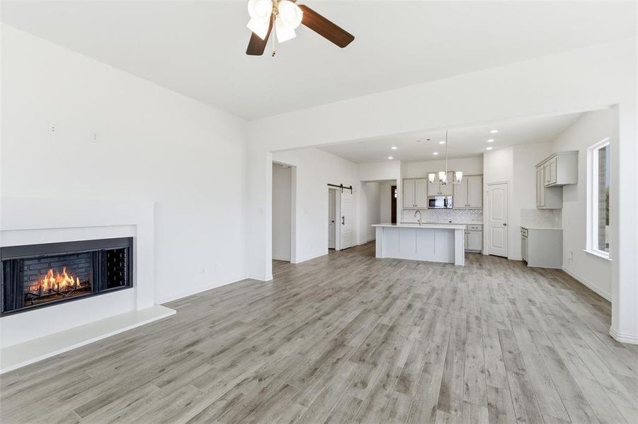 Unfurnished living room with a ceiling fan, hanging lights, a lit fireplace, and light wood-type flooring