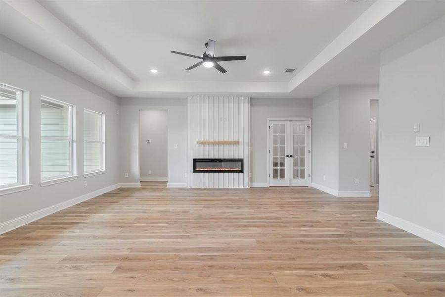 Unfurnished living room featuring a large fireplace, ceiling fan, light hardwood / wood-style floors, and a raised ceiling