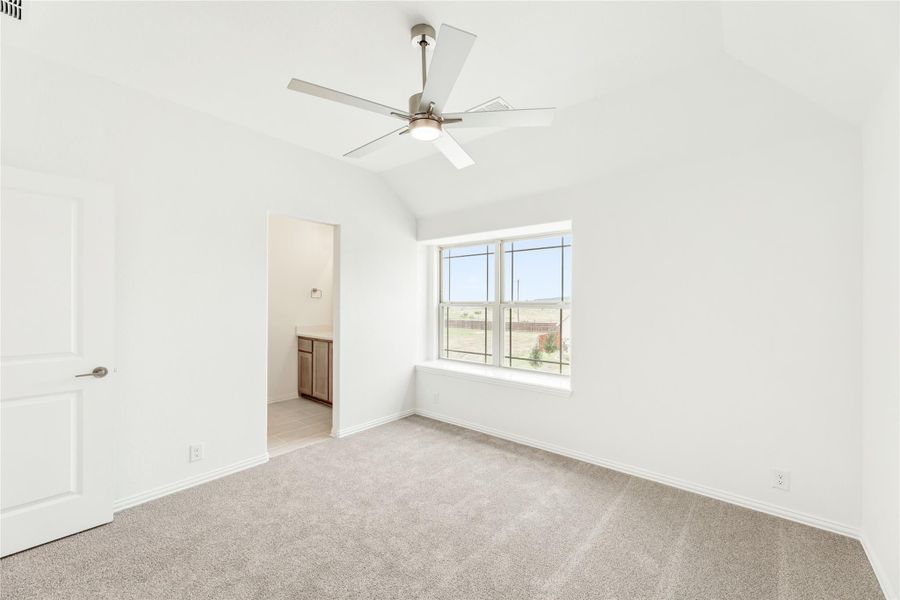 Empty bedroom with vaulted ceiling, ceiling fan, carpet, and ensuite bathroom doorway