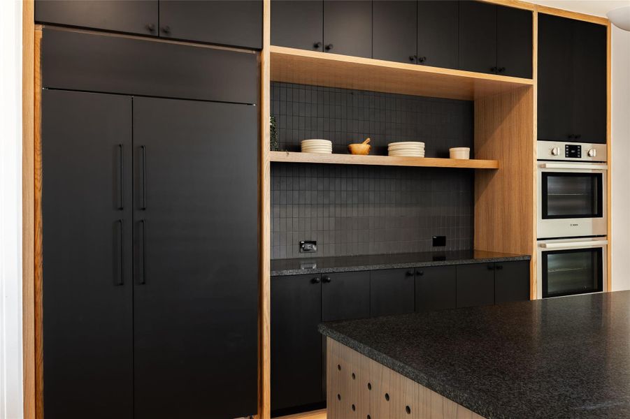 Kitchen with paneled refrigerator, dark cabinets, stainless steel double oven, decorative backsplash, and open shelves
