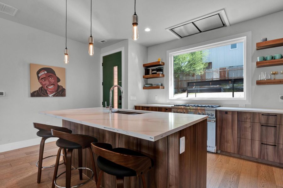 Kitchen with open shelves, high end range, modern cabinets, light wood finished floors, and a breakfast bar
