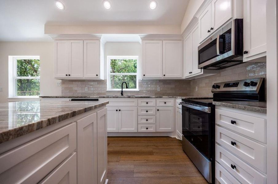 Kitchen featuring appliances with stainless steel finishes, white cabinetry, tasteful backsplash, light stone counters, and recessed lighting