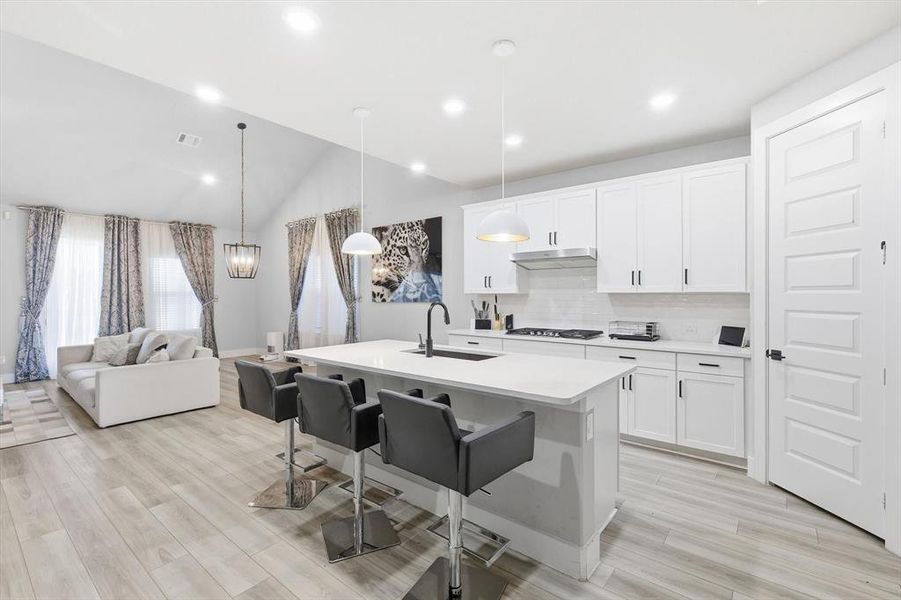 Kitchen featuring hanging light fixtures, backsplash, a breakfast bar area, white cabinetry, and open floor plan