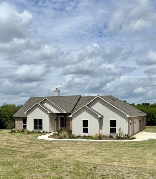 View of front facade featuring a shingled roof, a front yard, a chimney, covered porch, and an attached garage