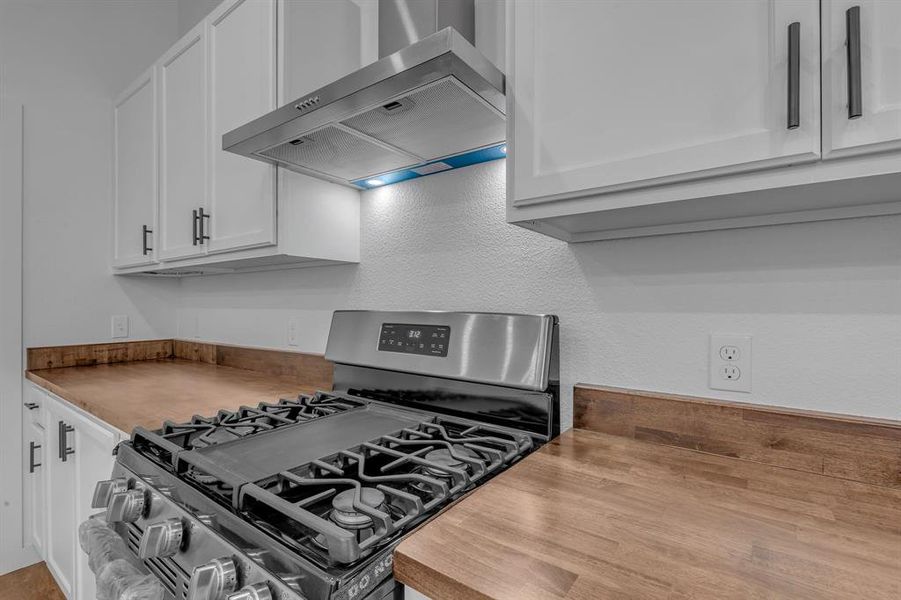 Kitchen featuring white cabinets, wall chimney exhaust hood, light wood-type flooring, and gas stove