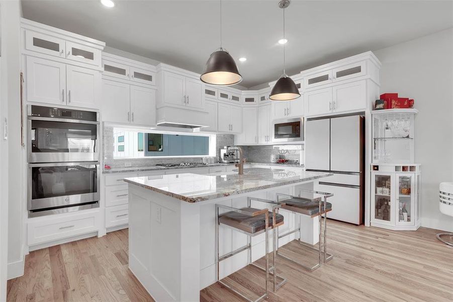 Kitchen with stainless steel appliances, a kitchen island, light stone counters, light hardwood / wood-style floors, and white cabinets