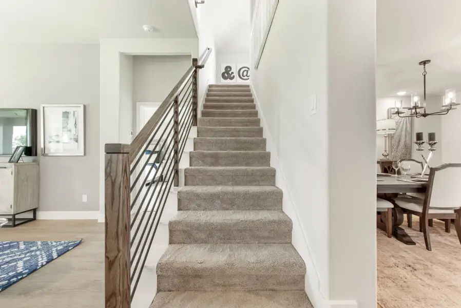 Carpeted staircase with wood and metal railing, dining room with chandelier visible to the right