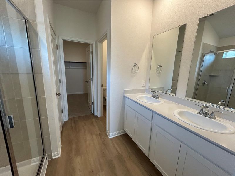 Full bath with a stall shower, dark wood finished floors, double vanity, a spacious closet, and a textured wall Full bath with a stall shower, dark wood finished floors, double vanity, a spacious closet, and a textured wall