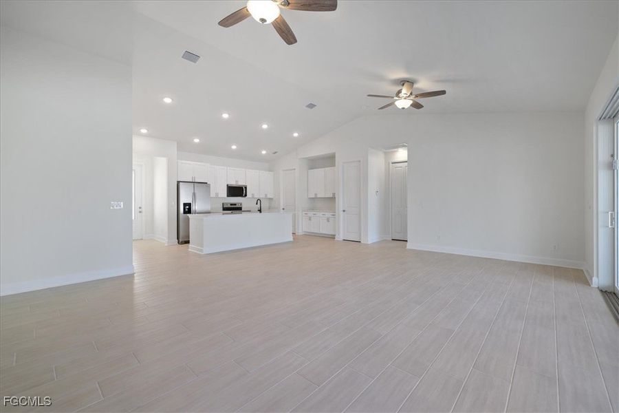 Unfurnished living room with lofted ceiling, light wood-style floors, ceiling fan, and recessed lighting Unfurnished living room with lofted ceiling, light wood-style floors, ceiling fan, and recessed lighting