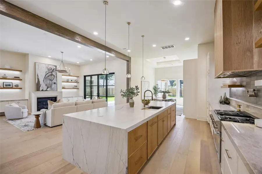 KITCHEN II: This beautifully appointed kitchen offers an expansive Taj Mahal quartzite island with deep undermount sink, custom wood vent hood, premium Thermador appliances, pot filler, and seamless sightlines into the living and dining areas.