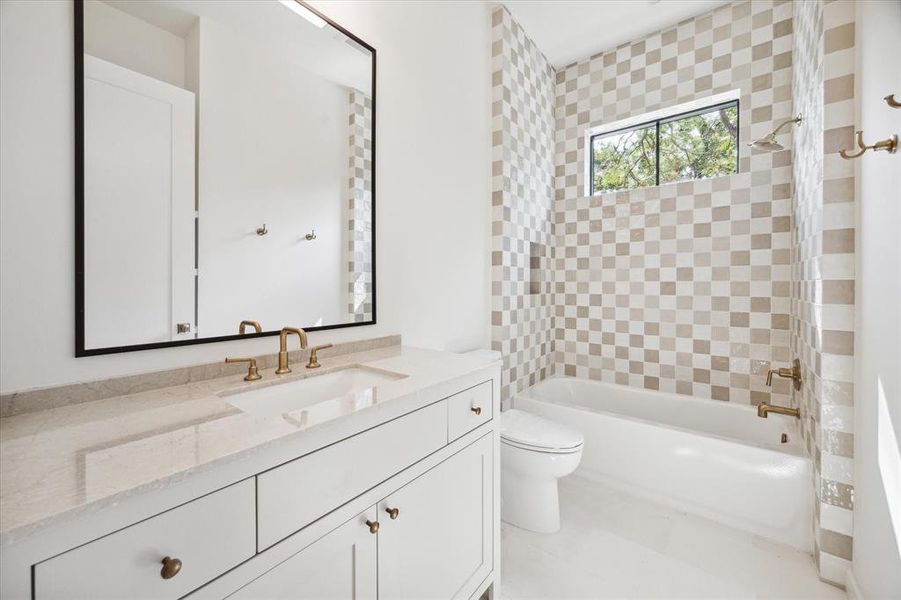 This secondary bathroom combines classic design with timeless touches. The shower-tub combo stands out with its eye-catching checkered tile in neutral tones, complemented by a small, high window that lets in natural light. The combination of clean lines and warm tones creates a space that feels both fresh and inviting.