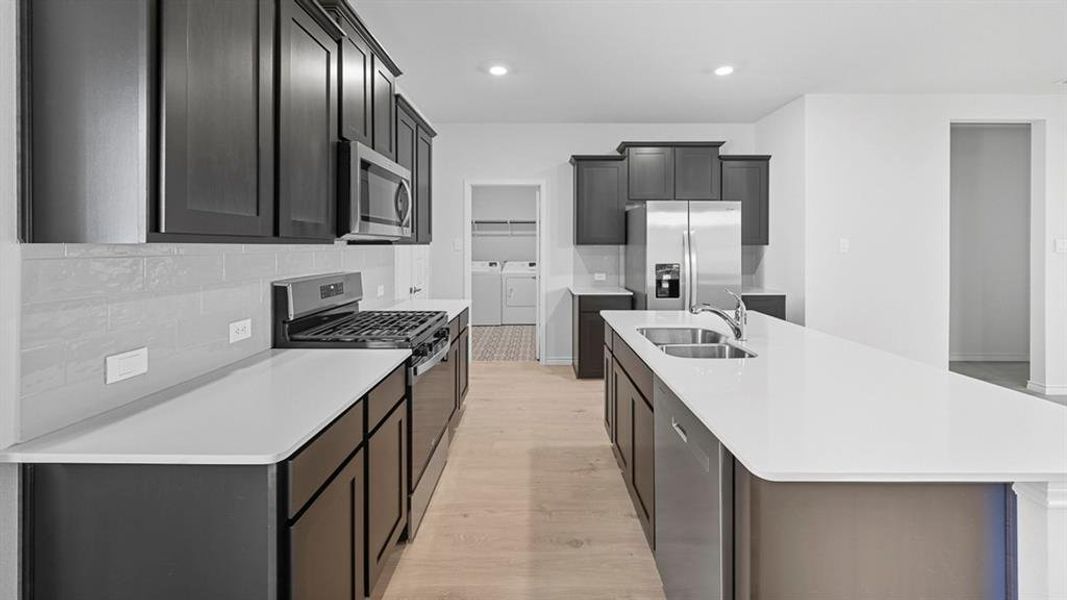 Kitchen with stainless steel appliances, backsplash, washing machine and clothes dryer, a kitchen island with sink, and light wood finished floors