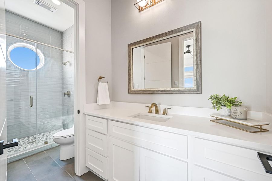 Natural light pours through the circular window, highlighting the elegant shower and spacious vanity area. Every detail was selected to create a relaxing spa inspired experience.
