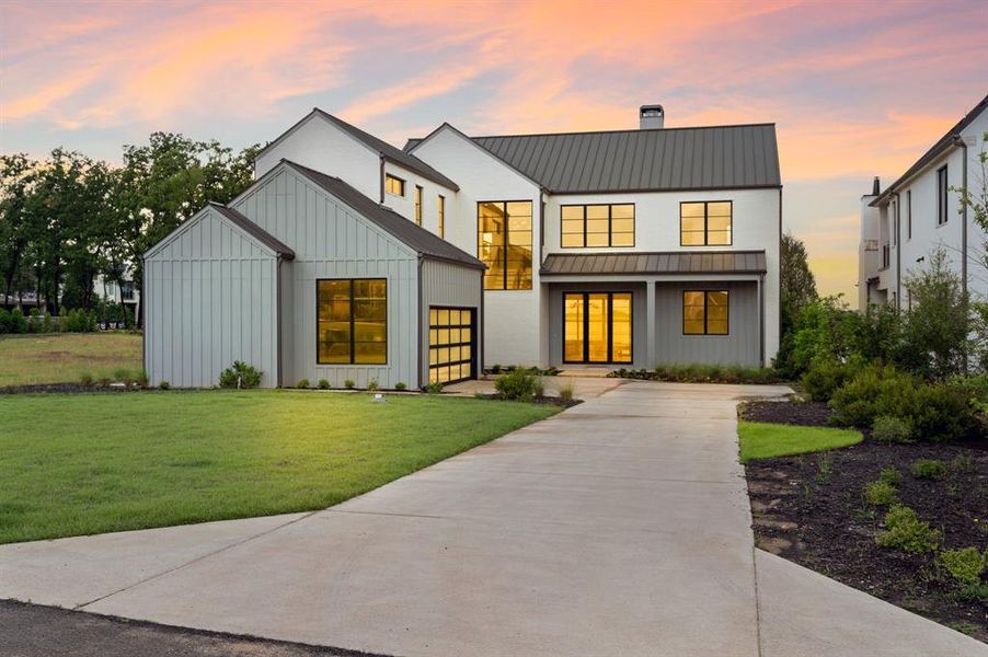Modern farmhouse with a standing seam roof, concrete driveway, board and batten siding, a chimney, and a front yard Modern farmhouse with a standing seam roof, concrete driveway, board and batten siding, a chimney, and a front yard