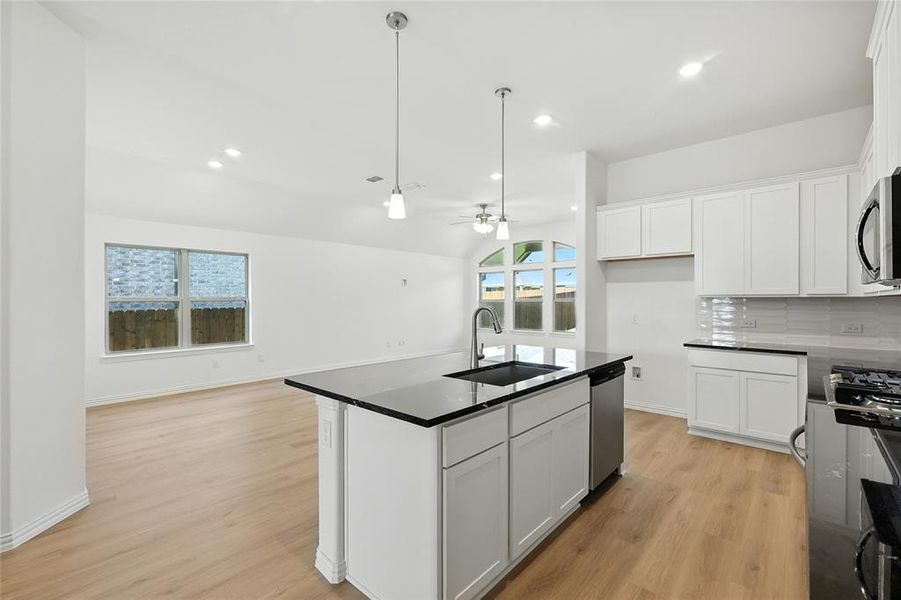 Kitchen with an island with sink, white cabinets, a ceiling fan, open floor plan, and light wood-style floors