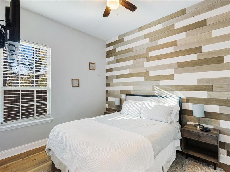 Bedroom with an accent wall, a ceiling fan, wooden walls, and wood finished floors