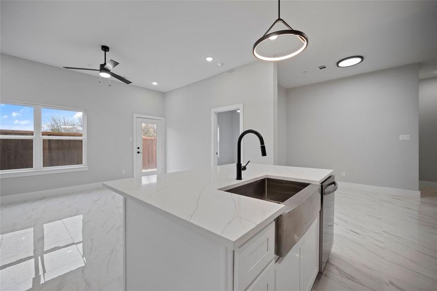 Kitchen featuring light stone countertops, open floor plan, dishwasher, marble finish floor, and a sink