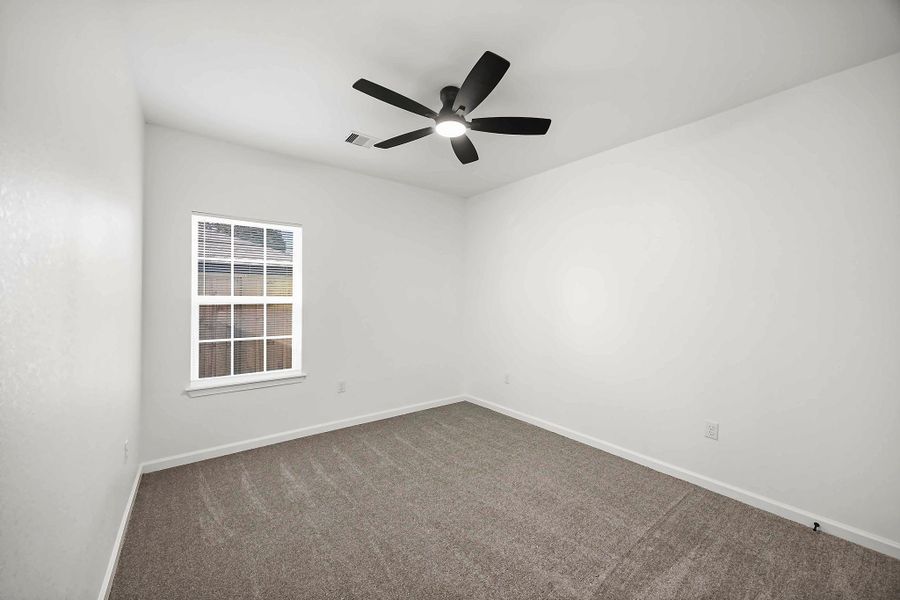 Bright and spacious room featuring fresh carpeting, a modern ceiling fan, and ample natural light from a large window.