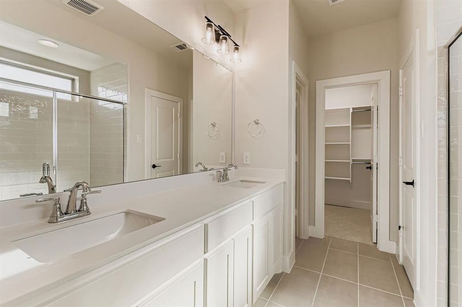 Full bathroom featuring double vanity, a shower stall, tile patterned floors, and a walk in closet
