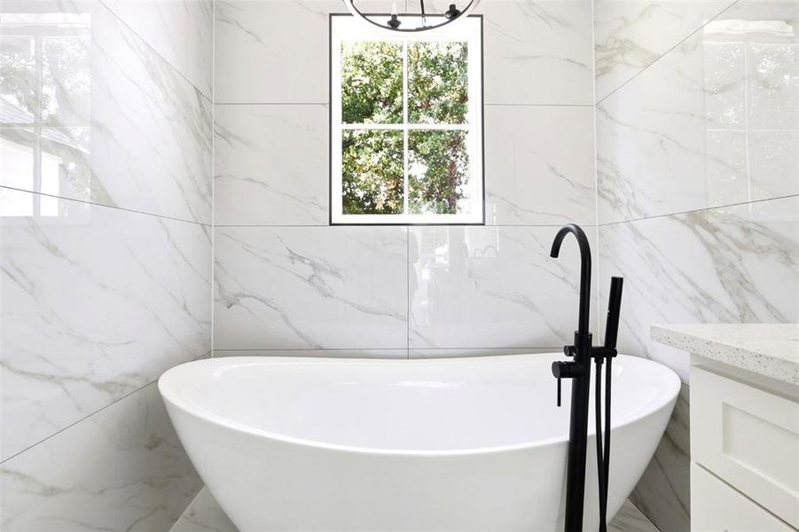Freestanding soaking tub with a matte black floor-mounted faucet and handheld shower sprayer