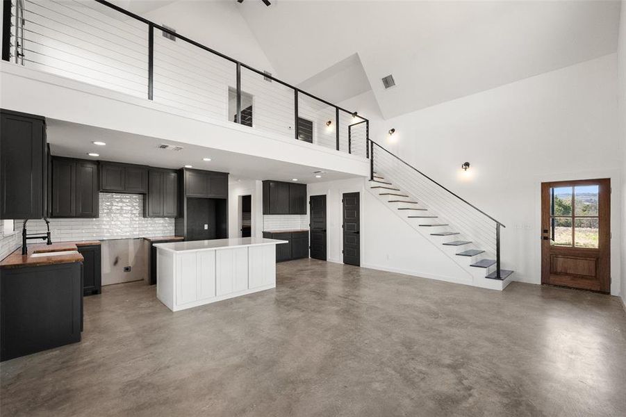 Kitchen with a center island, open floor plan, concrete flooring, dark cabinets, and backsplash