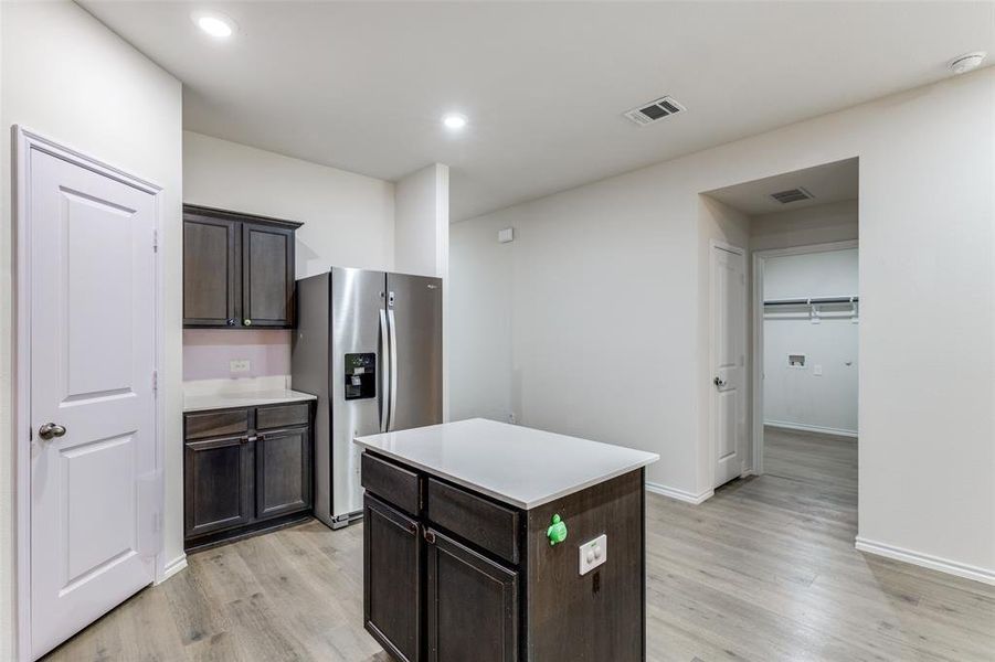 Kitchen featuring a central island with countertop, dark wood-finish cabinetry, stainless steel refrigerator, and wood-finish flooring Kitchen featuring a central island with countertop, dark wood-finish cabinetry, stainless steel refrigerator, and wood-finish flooring