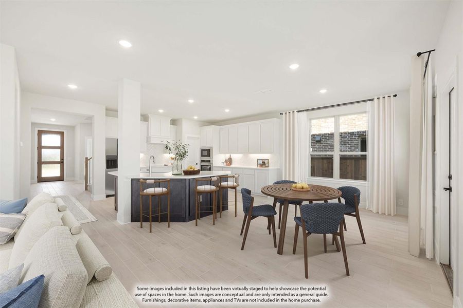 Open-concept living area with white kitchen, dark island, dining table, and light wood floors