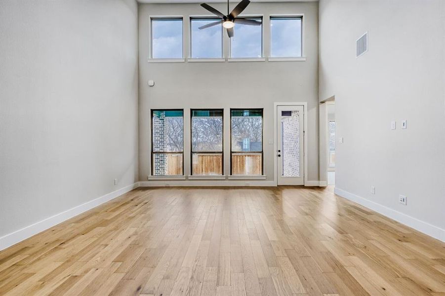 Unfurnished living room featuring a ceiling fan, light wood-style flooring, and a high ceiling
