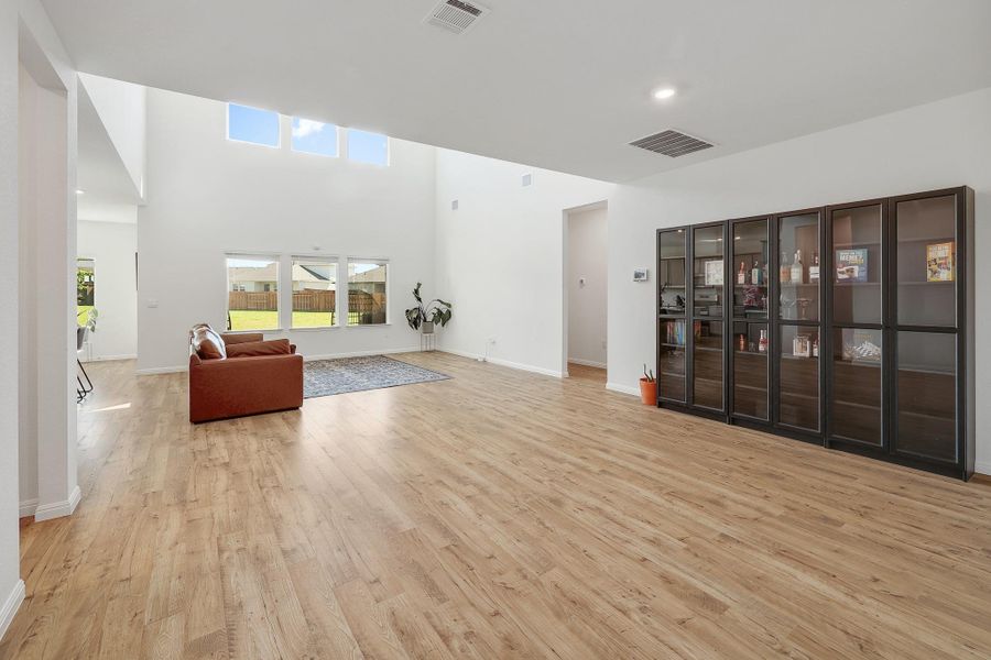 Spacious living area featuring high ceilings, wood-finish flooring, and multiple windows Spacious living area featuring high ceilings, wood-finish flooring, and multiple windows