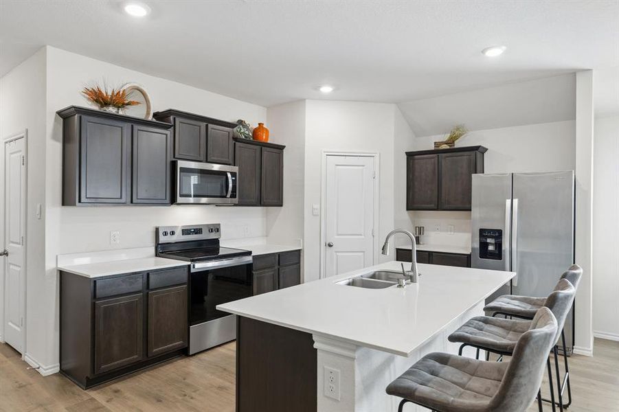 Kitchen with stainless steel appliances, light wood-style flooring, a center island with sink, dark wood finish cabinetry, and a breakfast bar area Kitchen with stainless steel appliances, light wood-style flooring, a center island with sink, dark wood finish cabinetry, and a breakfast bar area