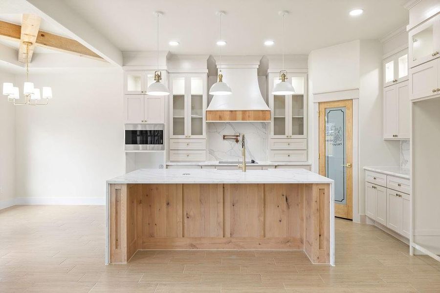 Kitchen featuring light wood finished floors, decorative backsplash, white cabinets, oven, and premium range hood