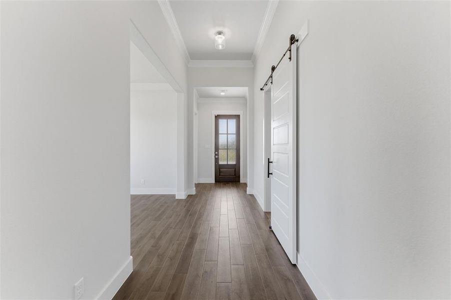 Hall featuring a barn door, ornamental molding, and dark wood-style flooring