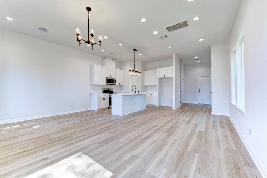 Expansive open-concept layout with wood-look LVP flooring, tall ceilings, and abundant recessed lighting throughout. Seamless flow from living to kitchen, anchored by a central island and complemented by clean white cabinetry and modern fixtures.