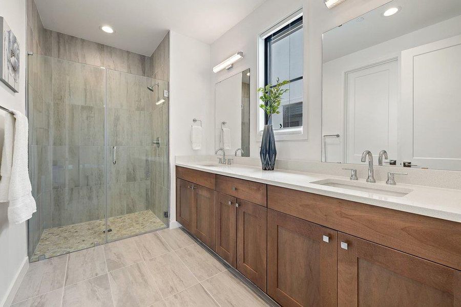 Contemporary bathroom featuring a spacious glass-enclosed shower with stone tile flooring, a dual vanity with light-toned countertops and wood-finish cabinetry, and a large window