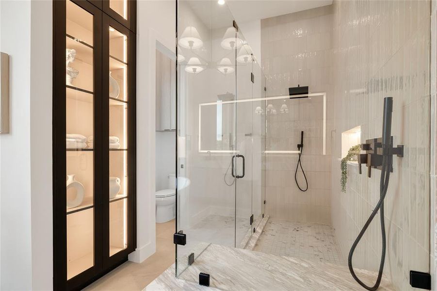 Glass-enclosed shower with matte black fixtures, integrated shelving, and textured tile walls Glass-enclosed shower with matte black fixtures, integrated shelving, and textured tile walls