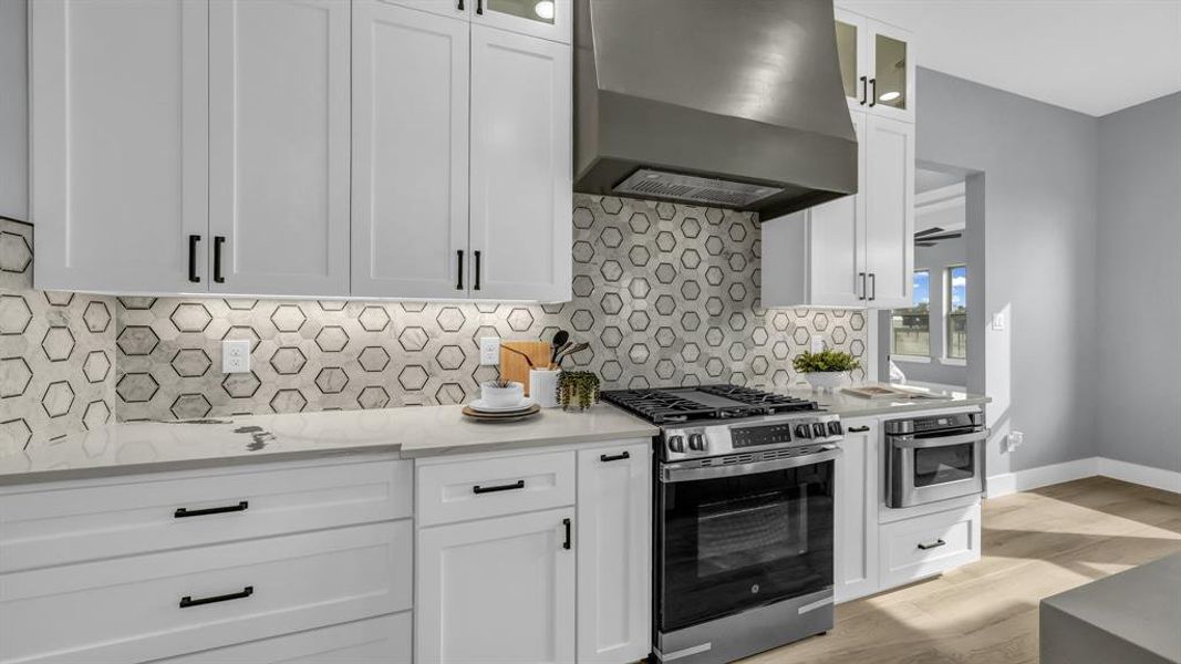 Kitchen with glass insert cabinets, stainless steel appliances, extractor fan, and white cabinetry
