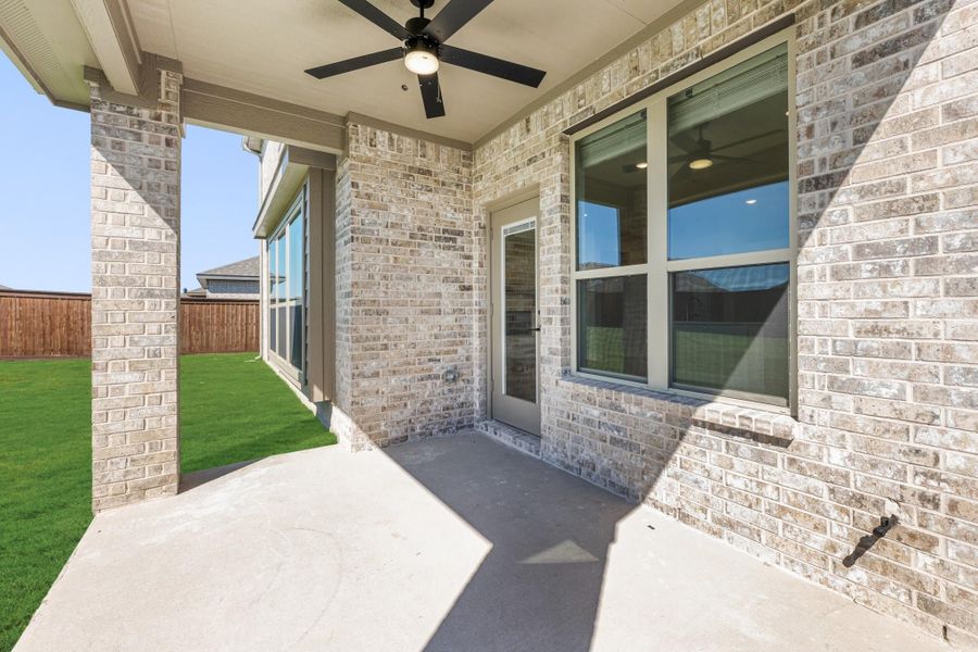 Covered back patio with ceiling fan, brick exterior, concrete floor, and fenced backyard with green lawn