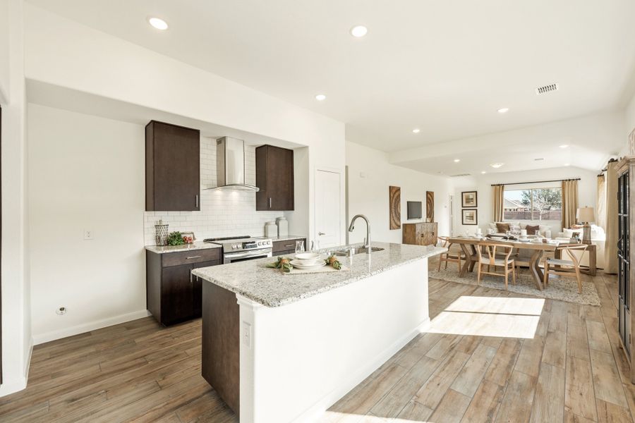 Open-concept kitchen with granite island, dark cabinets, and wood-look floors flowing into dining and living areas